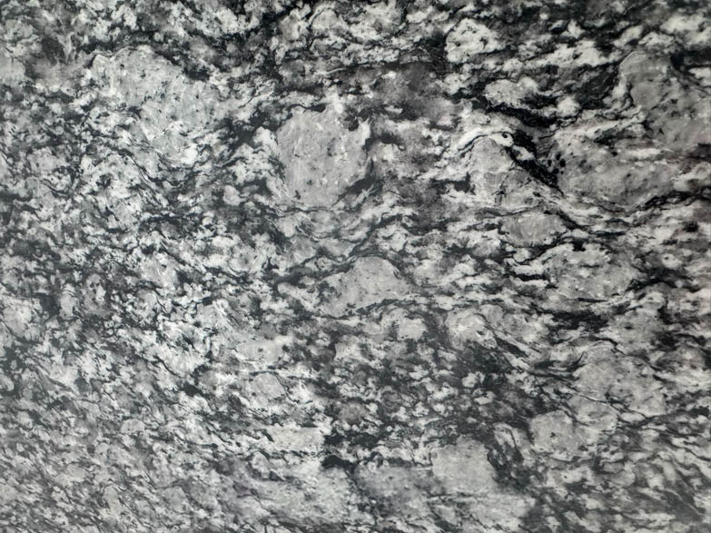 Close-up of a textured gray and black granite surface with swirling patterns and speckles throughout, creating a marbled, natural stone appearance.