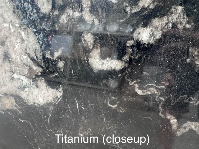 A close-up image of a titanium surface with swirling, marble-like patterns in shades of black, white, and gray. The caption at the bottom reads Titanium (closeup).