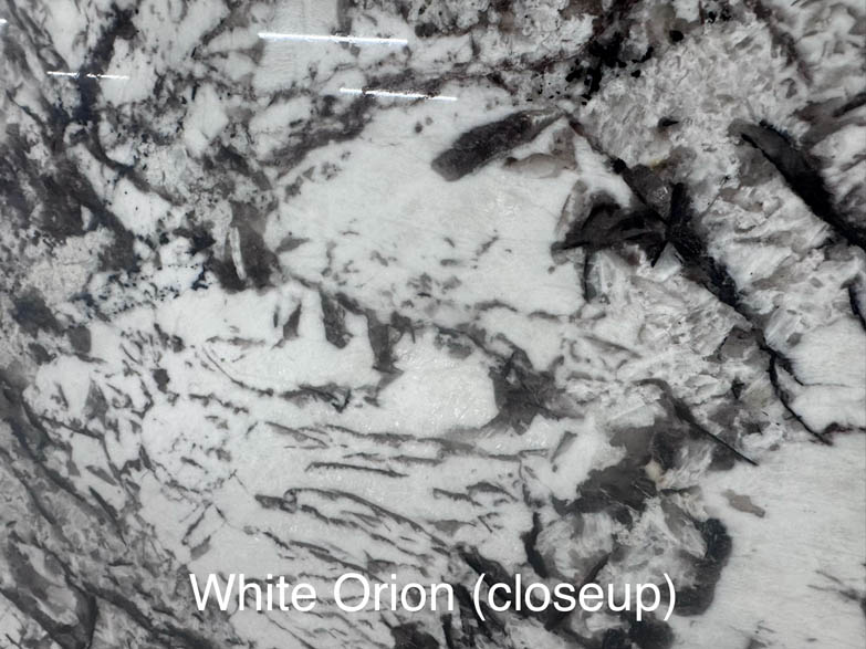 Closeup of a White Orion granite surface, showing a mix of white, gray, and black streaks and patterns. The text White Orion (closeup) is overlaid at the bottom of the image.